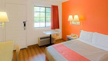 A hotel room with a bed, a desk, a chair, a window with curtains, and a wall-mounted lamp.