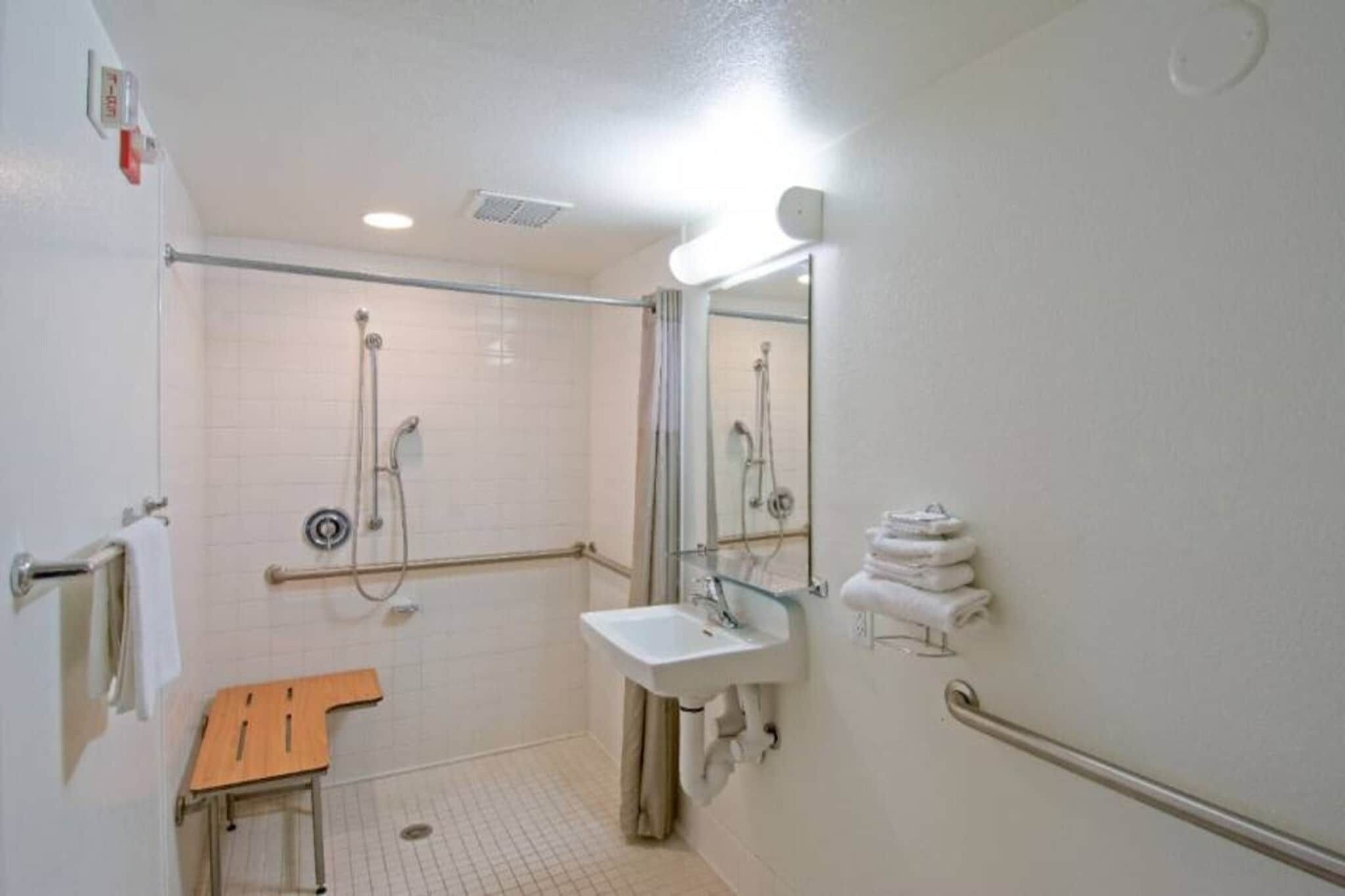 A bathroom with a shower, sink, and handrails.