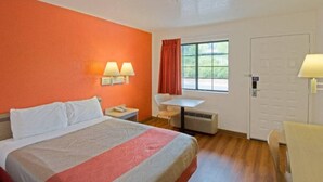 Ett hotellrum med en säng, ett skrivbord, två lampor, en stol och ett fönster med gardiner.