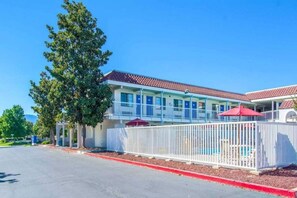 A motel with a fenced pool area, a covered patio, and a clear blue sky. - 1 Queen Bed | Micfridge (Redding CA)