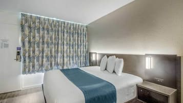 A modern hotel room with a large bed, a headboard with integrated lighting, a bedside table, and a patterned curtain.