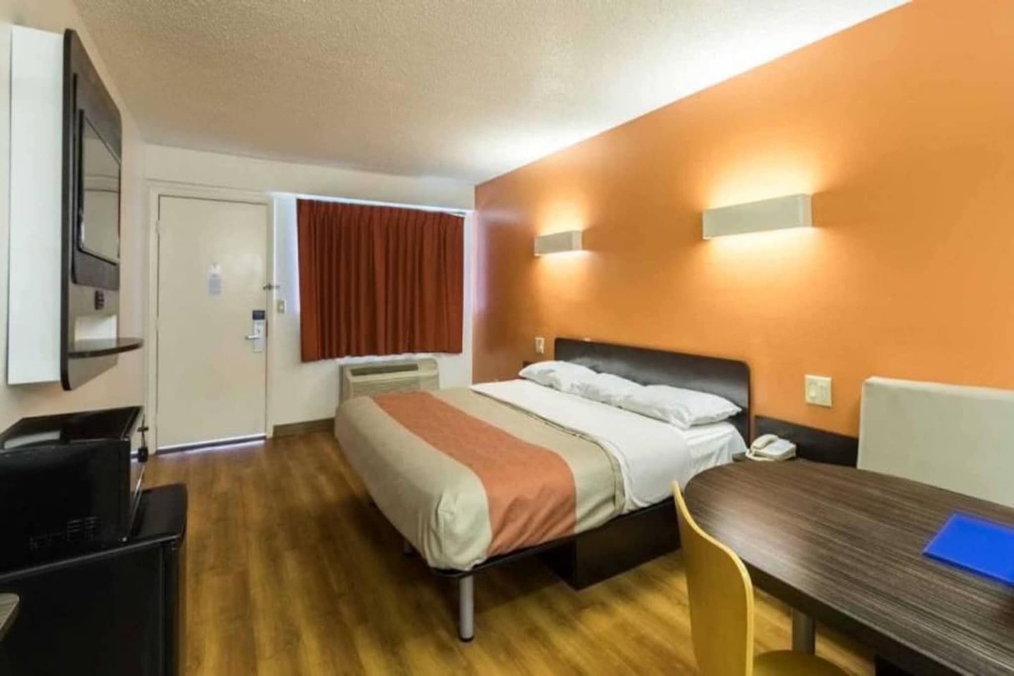 A hotel room with a bed, a desk, a chair, a TV, and a window with curtains.