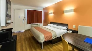 Una habitación de hotel con cama, escritorio, silla, televisor y ventana con cortinas.
