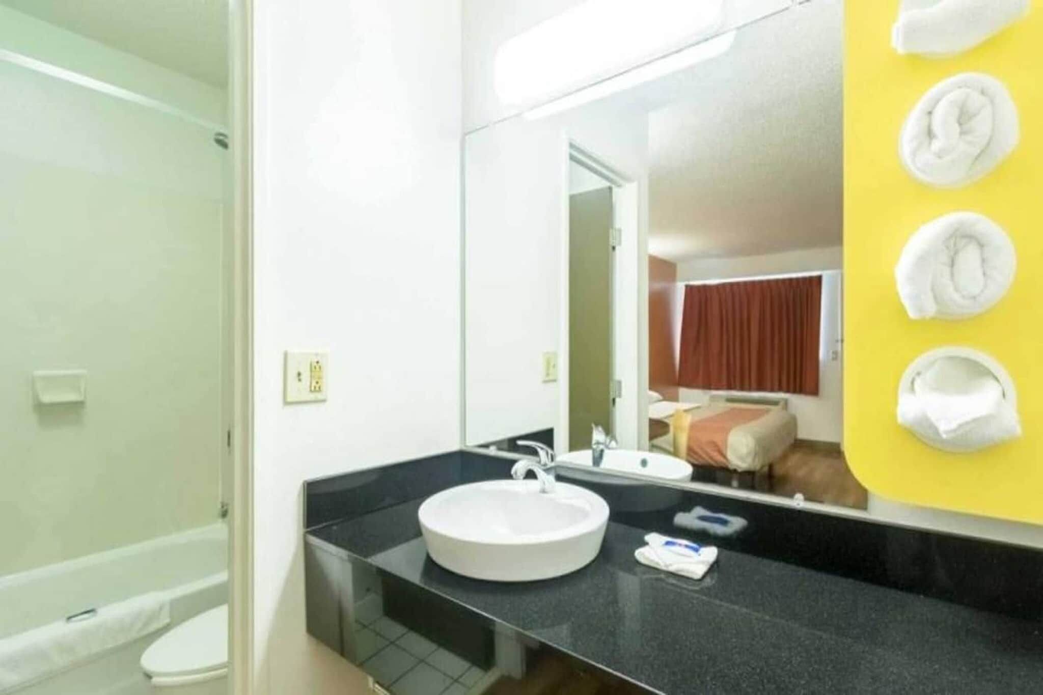 A bathroom with a round sink, a mirror, and a yellow towel rack.