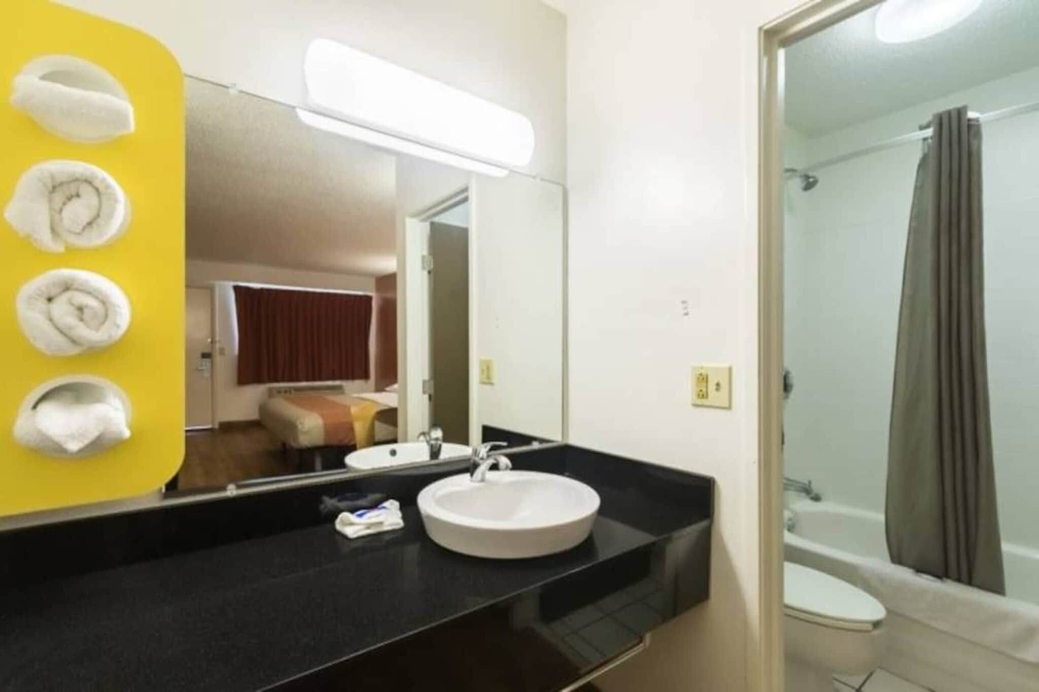 A hotel bathroom with a round sink, a mirror, and a shower area.