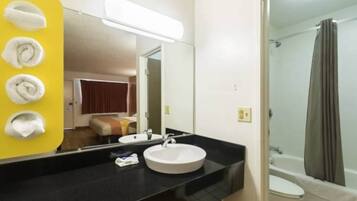 A hotel bathroom with a round sink, a mirror, and a shower area.