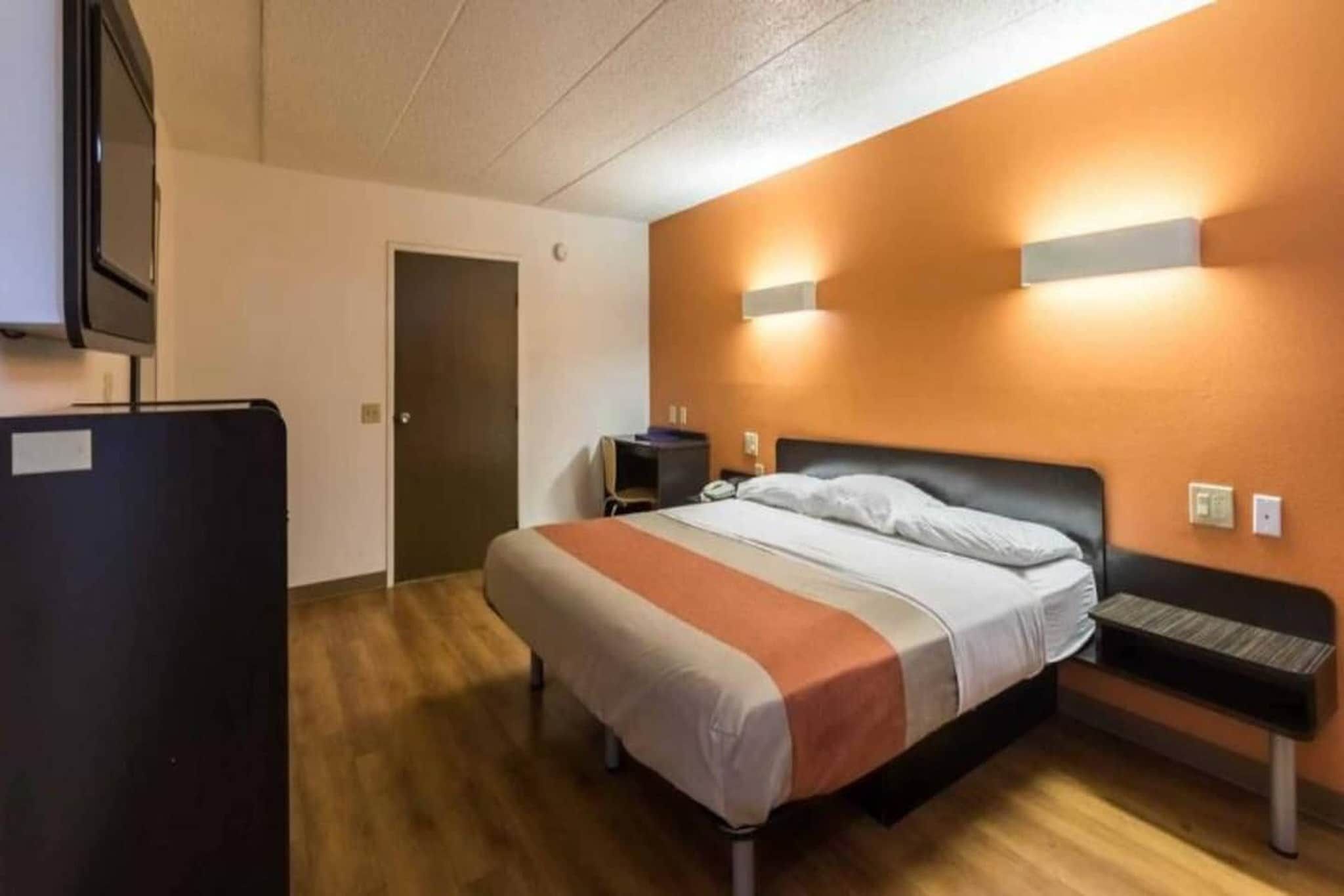 Et hotelværelse med en seng, et skrivebord, en stol, et fjernsyn og en dør.