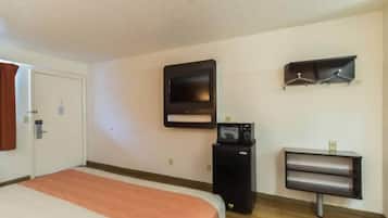 A hotel room with a bed, a television mounted on the wall, a small desk with a chair, and a coat rack.