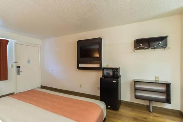 A hotel room with a bed, a television mounted on the wall, a small desk with a chair, and a coat rack.