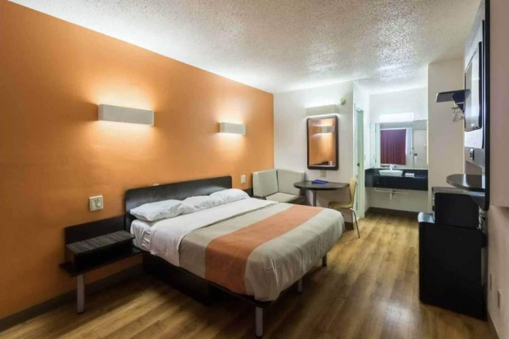 A hotel room with a bed, bedside table, chair, and a small desk with a mirror.
