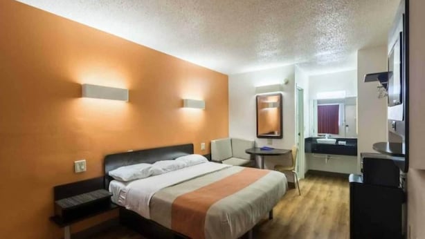 Una habitación de hotel con cama, mesita de noche, silla y un pequeño escritorio con espejo.