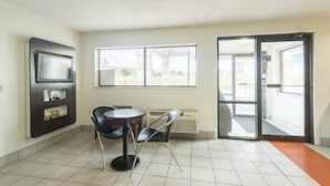 Una habitación con suelo de baldosas, una mesa con sillas, un televisor de pantalla plana en la pared y un amplio ventanal con vistas al exterior.