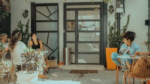 Un área de estar al aire libre con mesas y sillas, un amplio ventanal y plantas en macetas.