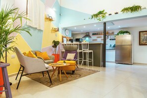 Una sala de estar moderna con un sofá, sillas y una mesa de centro. Hay una zona de cocina con un refrigerador y un microondas.