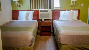 Een hotelkamer met twee bedden, een nachtkastje met een lamp, een airconditioning en een raam met gordijnen.
