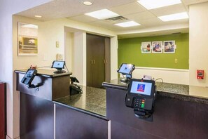 A reception area with two check-in counters, a fire alarm, and a green wall with framed pictures. - 2 Full Beds | Smoking (Greensboro)