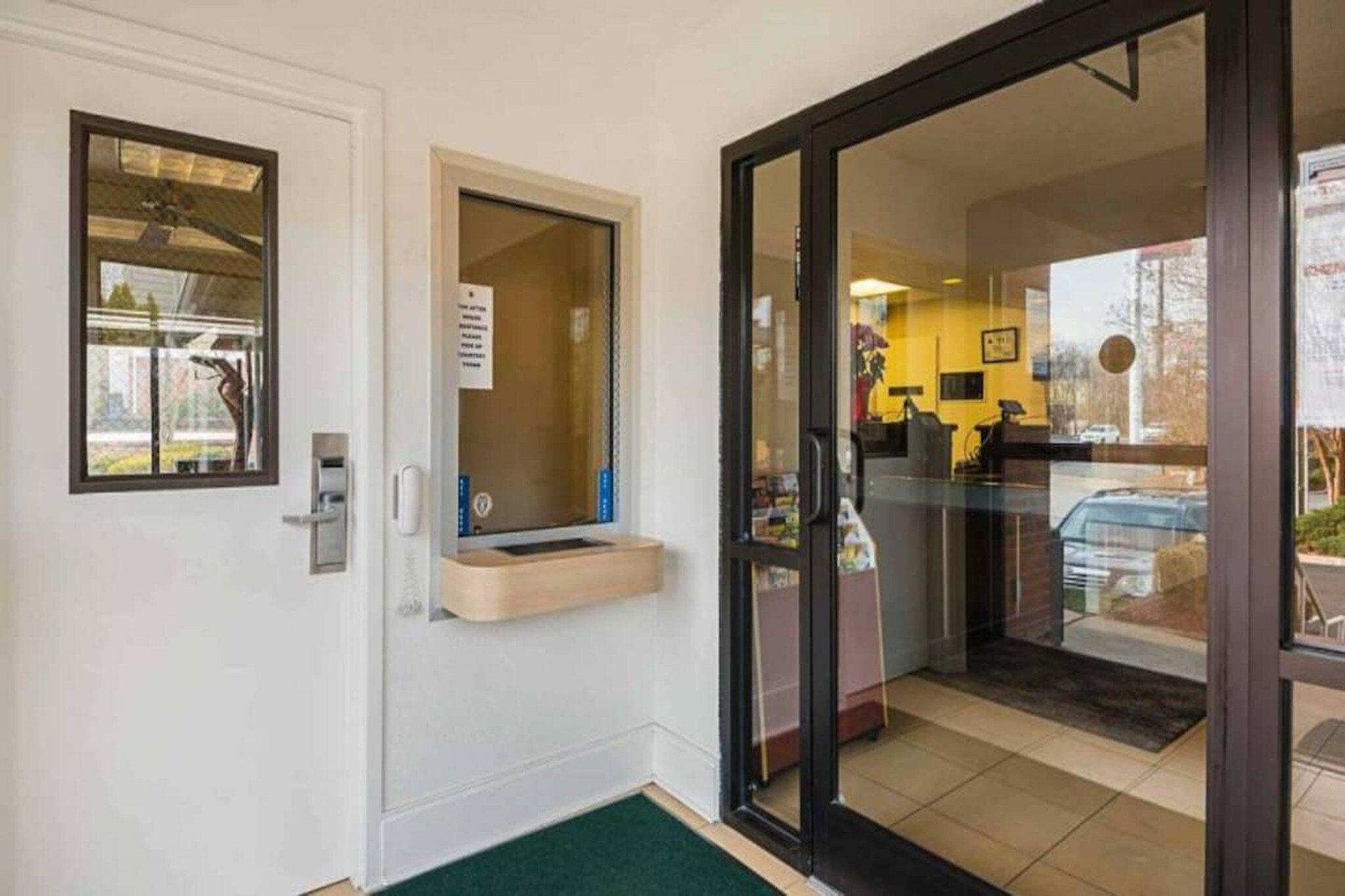 Entrada de un hotel con un mostrador de recepción, un ventanal pequeño y una puerta que da al interior.