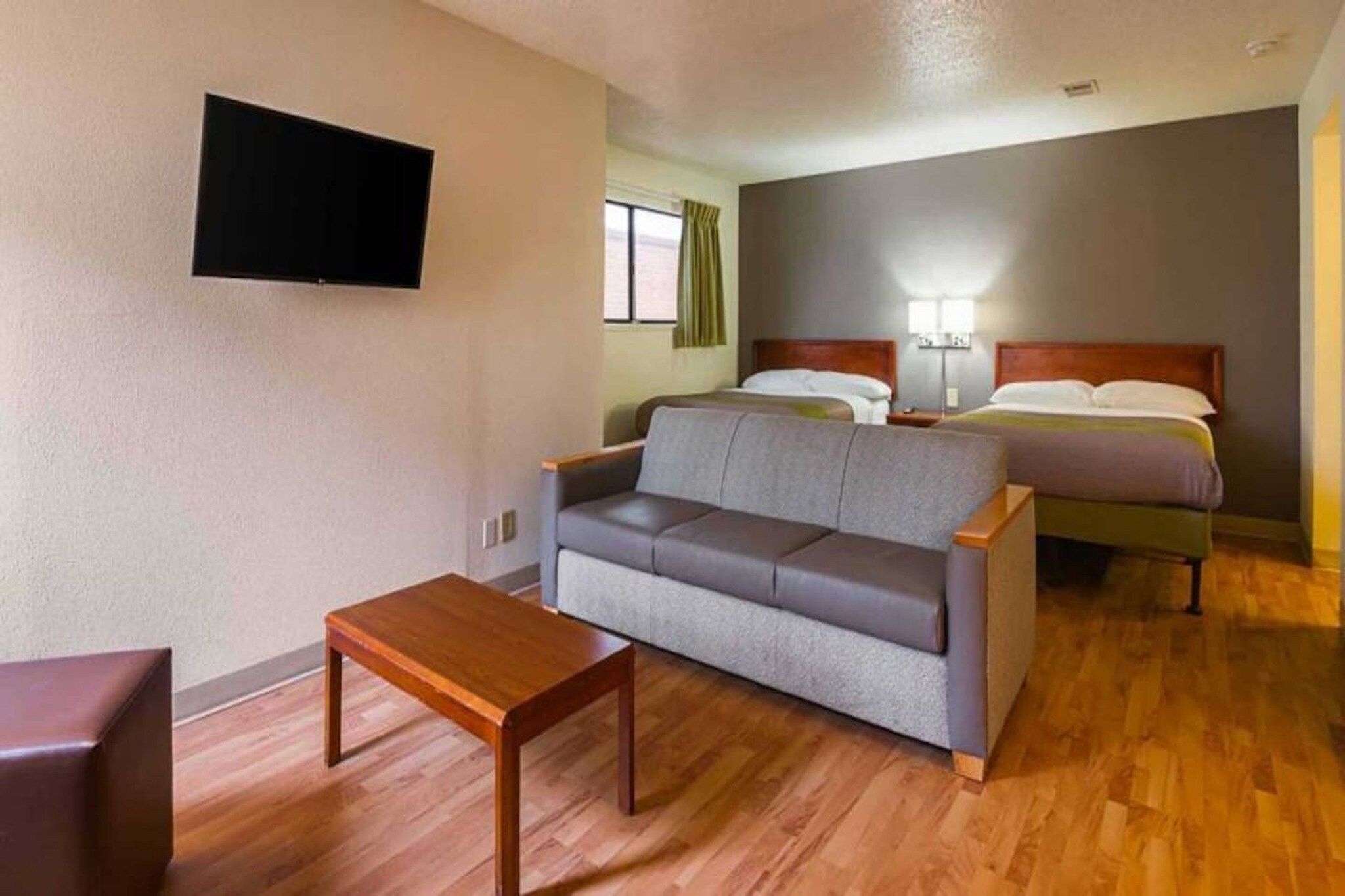 Ein Hotelzimmer mit einer Couch, einem Holztisch, einem Bett und einem an der Wand befestigten Fernseher.