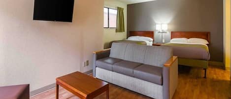 A hotel room with a sofa, a wooden table, a bed, and a TV mounted on the wall.