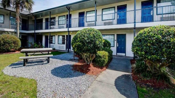 A two-story motel with a covered parking area, a picnic table, and well-maintained landscaping. - 2 Full Beds | Smoking (Ocean Springs)