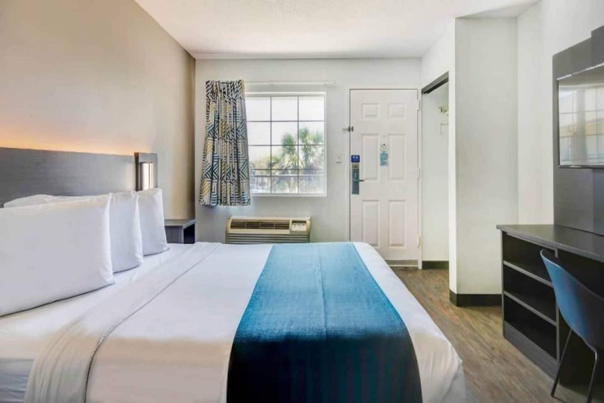Ein Hotelzimmer mit einem Bett, einem Schreibtisch, einem Sessel, einem Fenster mit Vorhängen und einer Tür.