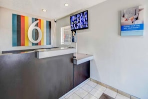 A reception desk with a modern design, a large number '6' on the wall, a television screen, and a poster advertising budget extension. - 2 Full Beds | Smoking (Ocean Springs)