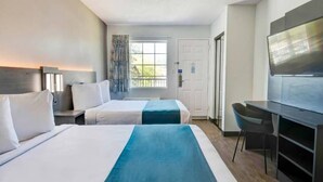 A hotel room with two beds, a desk, a chair, a television, and a window with a view of greenery. - 2 Full Beds | Smoking (Ocean Springs)