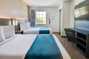 A hotel room with two beds, a desk, a chair, a television, and a window with a view of greenery. - 2 Full Beds | Smoking (Ocean Springs)