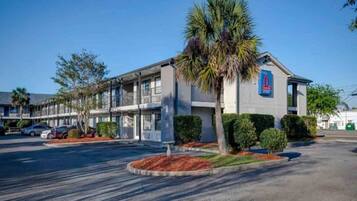 A motel with a parking lot, a palm tree, and a sign indicating the number of rooms.