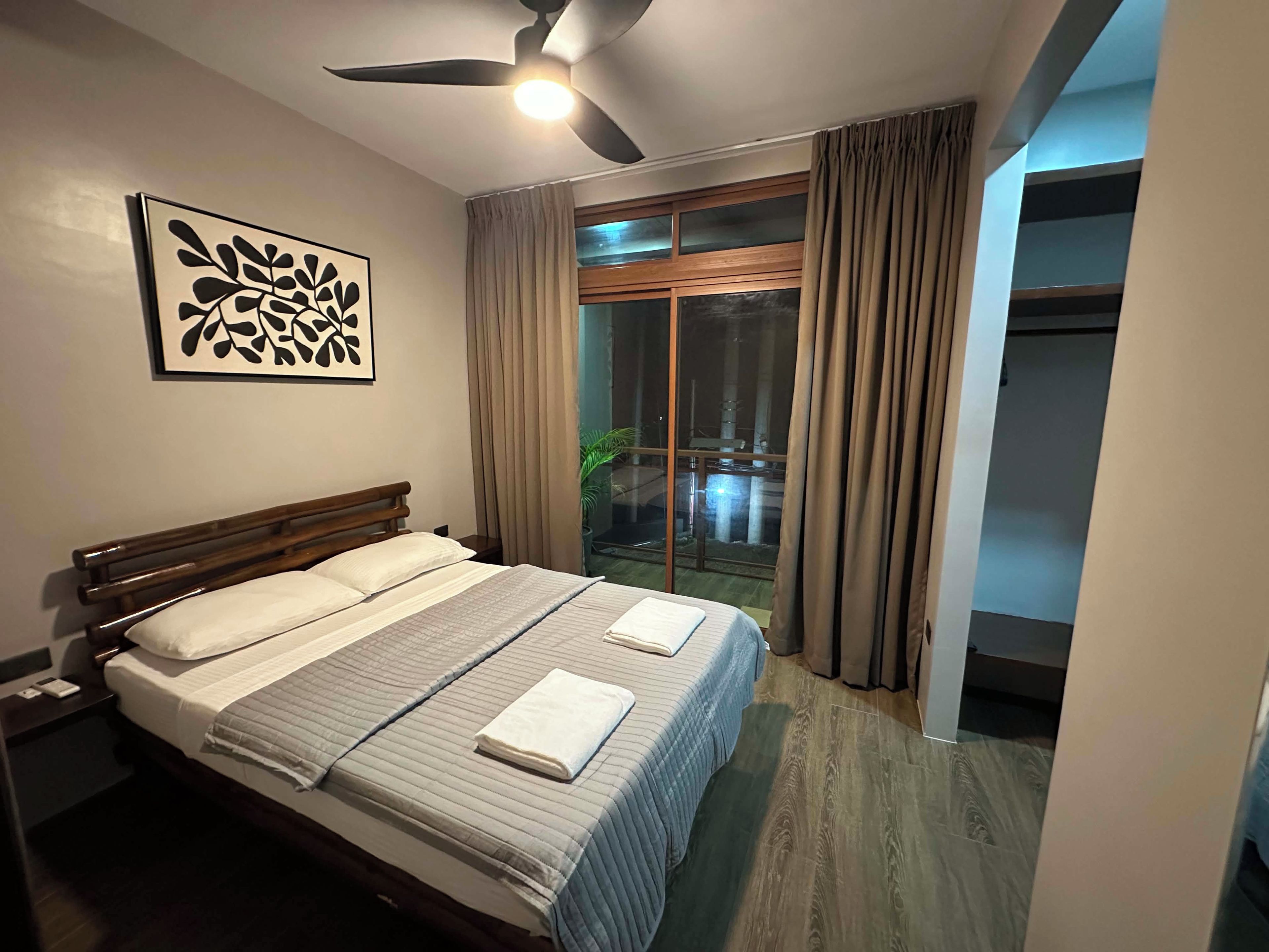 Une chambre d’hôtel avec un lit, un ventilateur de plafond, une fenêtre avec des rideaux et une vue sur l’extérieur.