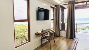 Ett rum med ett skrivbord, en stol, en tv, stora fönster och utsikt över havet.