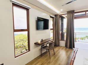 Ein Zimmer mit Schreibtisch, Stuhl, Fernseher, großen Fenstern und Meerblick.