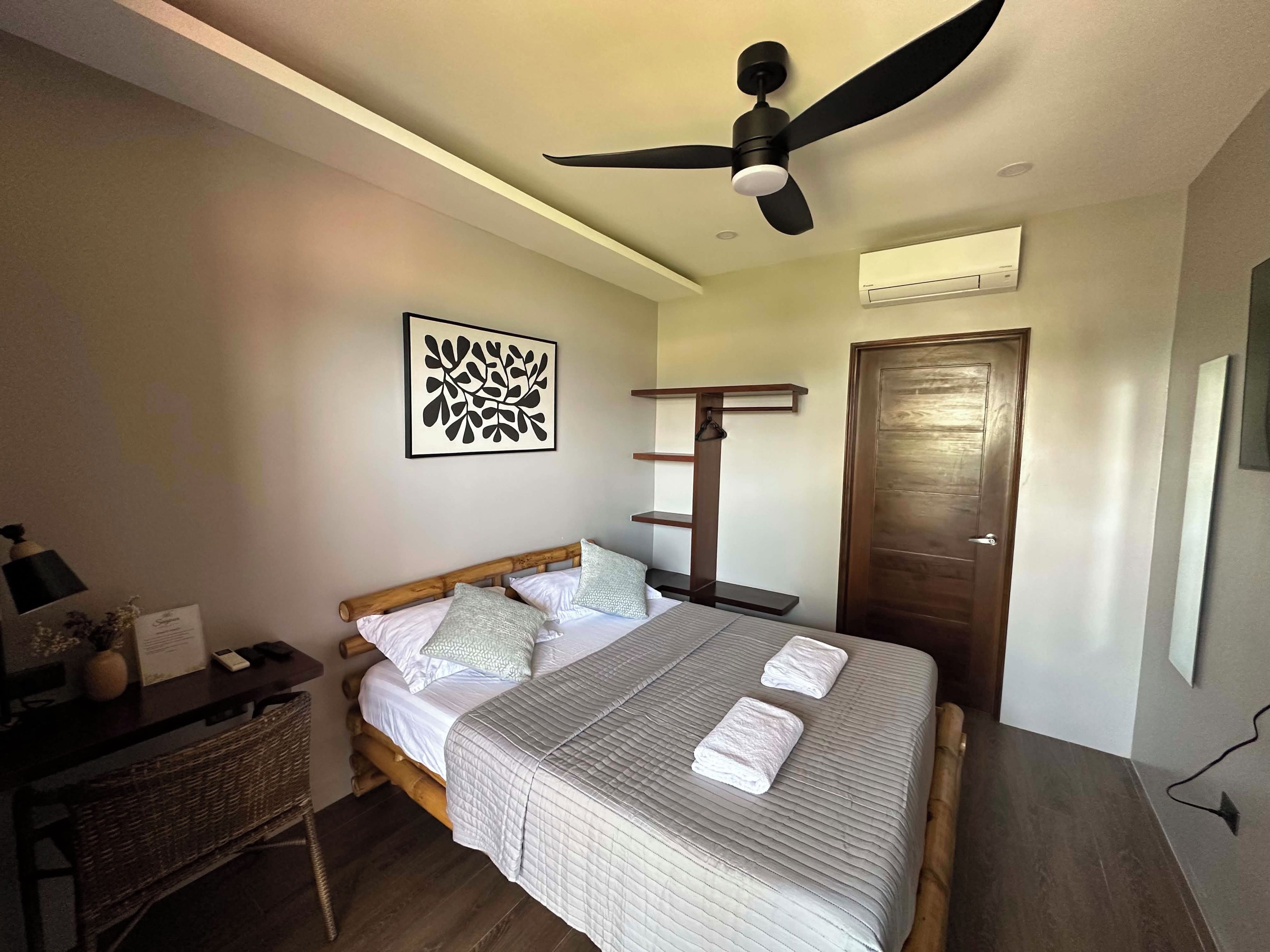 Une chambre à coucher comprenant un lit, un ventilateur de plafond, un climatiseur fixé au mur et une porte.