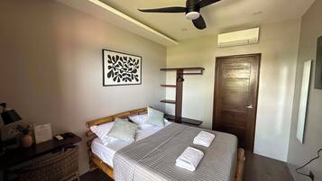 A bedroom with a bed, a ceiling fan, a wall-mounted air conditioner, and a door.
