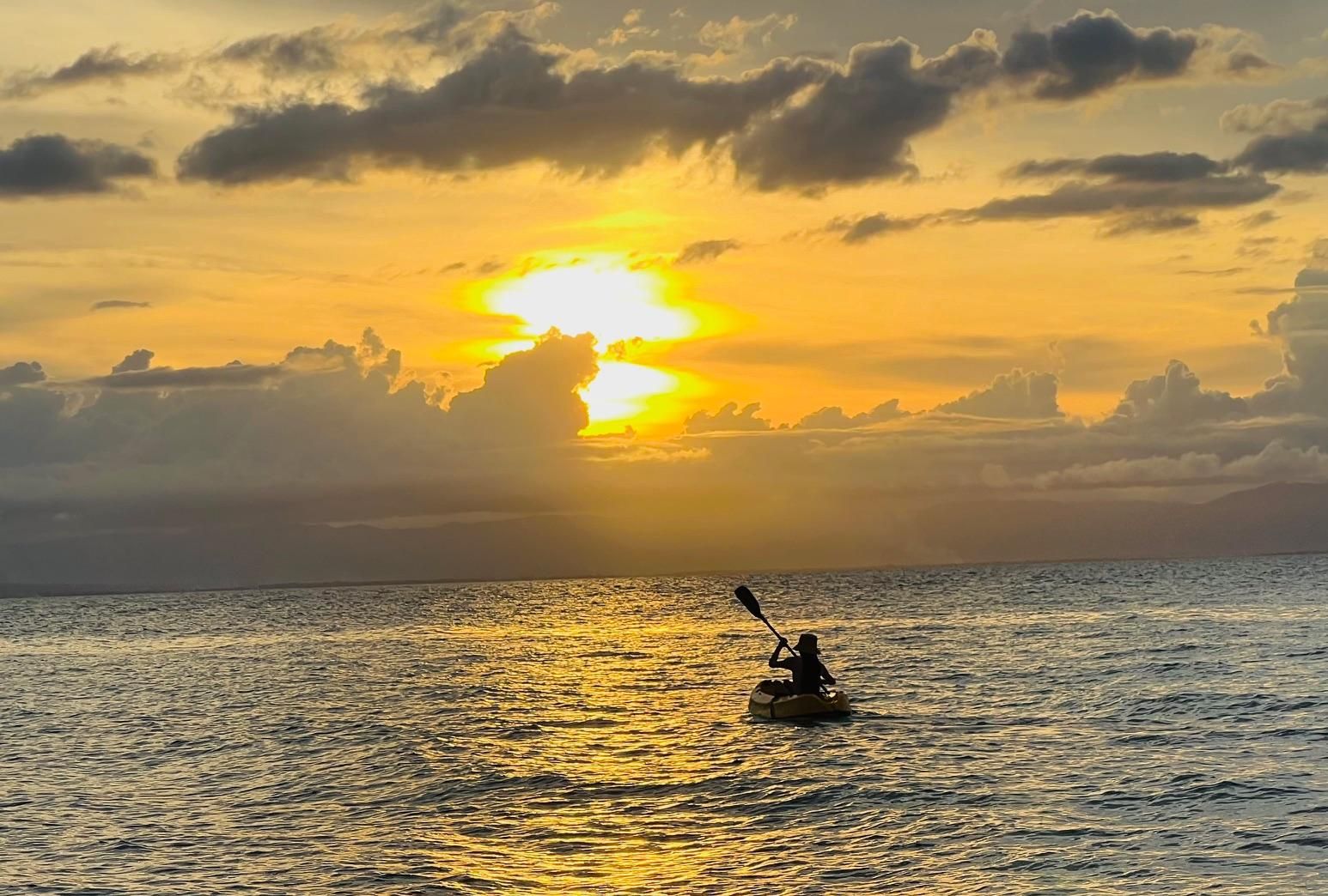 Un kayakiste sur une étendue d'eau calme, au coucher du soleil.