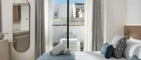 Una habitación de hotel con una cama, un espejo, una ventana con cortinas y vistas a edificios.