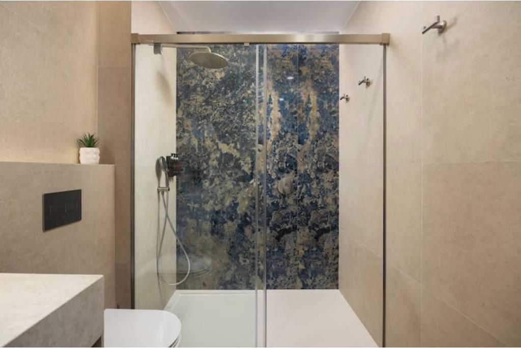 Un baño moderno con ducha envuelta en vidrio, lavamanos blanco y una pequeña planta en maceta.