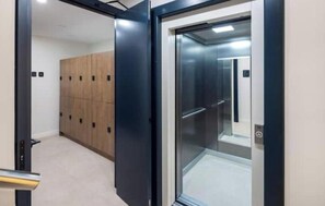 An elevator with a glass door, a wooden panel wall, and a metal handrail. - "Indigo" Apartment (Estepona)