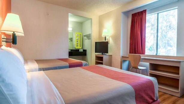 Een hotelkamer met twee bedden, een bureau met een computer, een televisie en een raam met gordijnen.