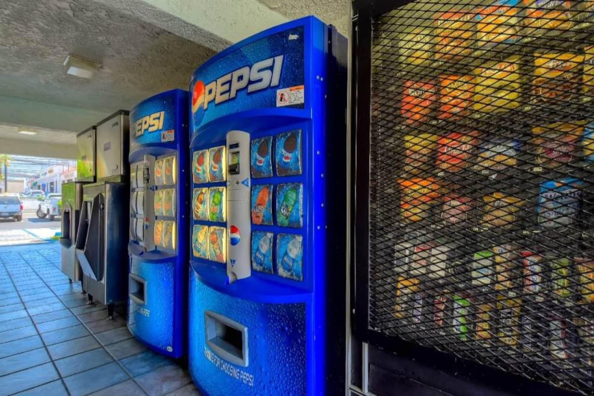 Una filera de màquines expenedores blaves amb el logotip de Pepsi, situades fora d'un edifici amb un sòl de rajola.