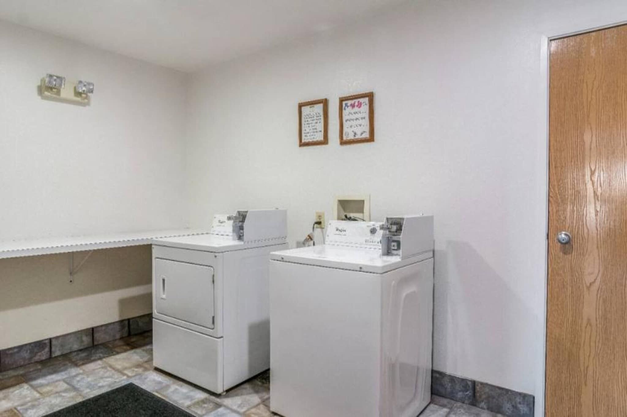 A laundry room with two washing machines and a dryer, a tiled floor, and a wooden door.