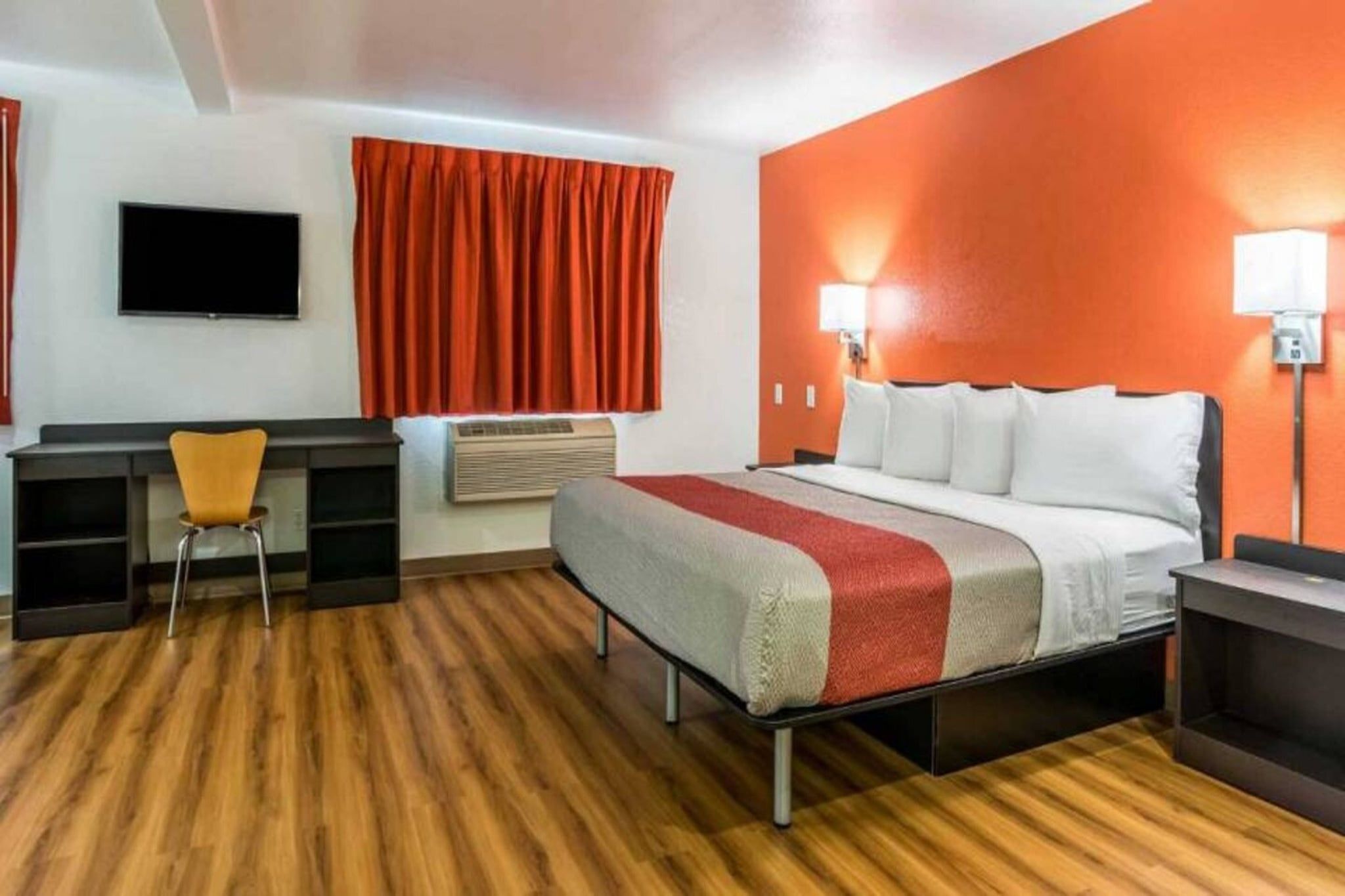 A hotel room with a bed, a desk, a chair, a TV, and a window with curtains.