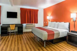 A hotel room with a bed, a desk, a chair, a TV, and a window with curtains.