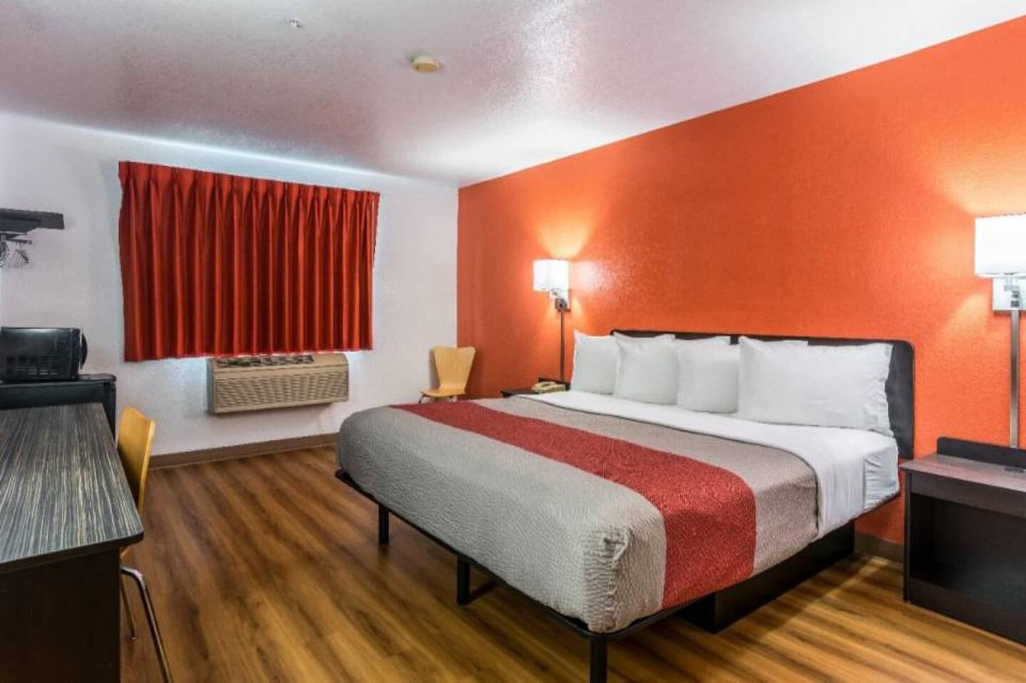 A hotel room with a bed, a desk, a chair, a lamp, and a window with curtains.