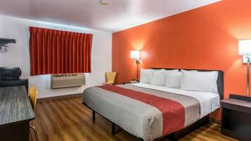 A hotel room with a bed, a desk, a chair, a lamp, and a window with curtains.