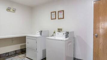 A laundry room with two washing machines and a dryer, a tiled floor, and a wooden door.
