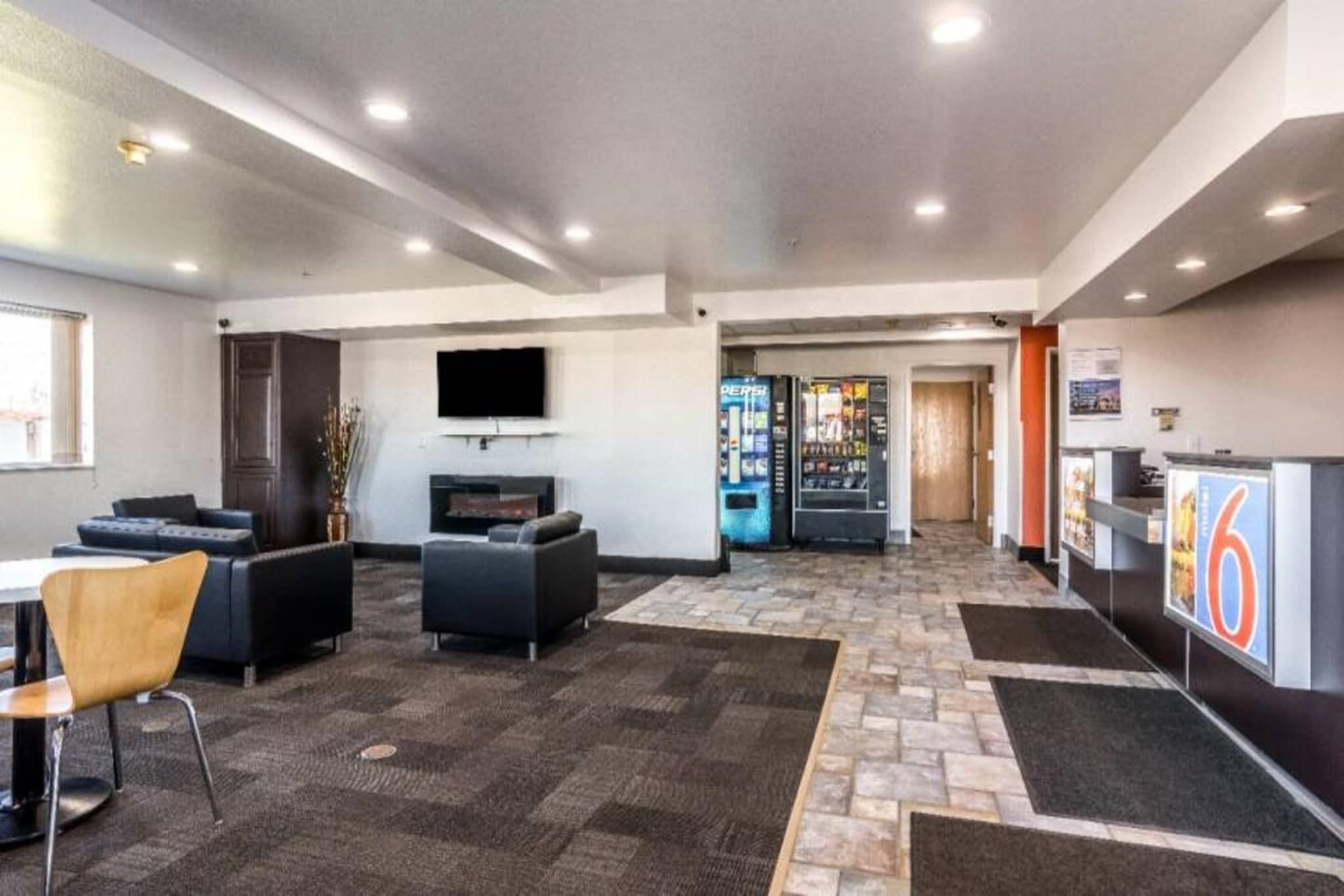 A hotel lobby with seating, a flat-screen TV, a vending machine, and a reception desk.