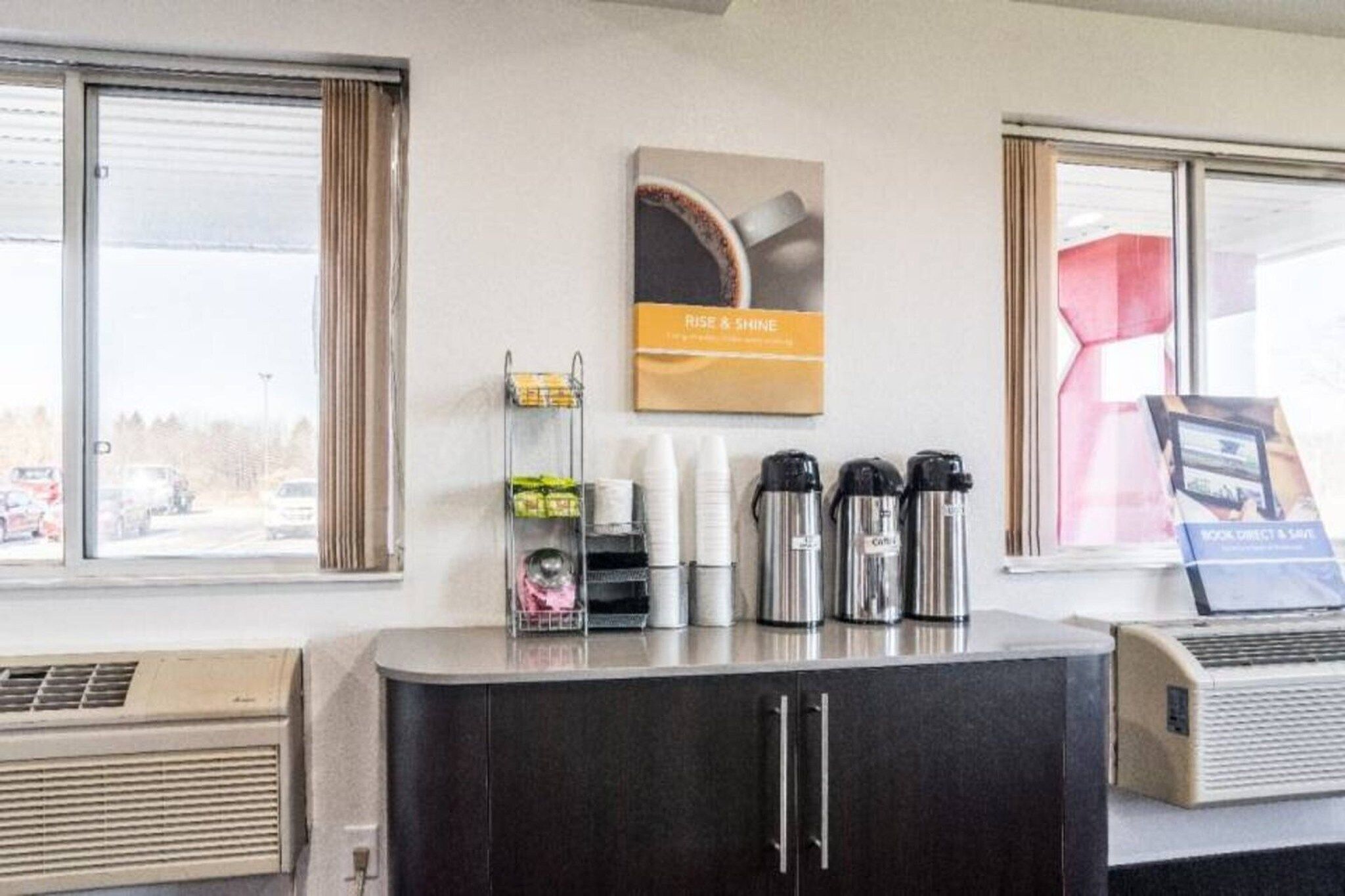 A hotel reception area with a counter, coffee makers, and a poster on the wall.