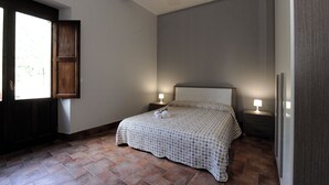 A bedroom with a bed, two bedside tables with lamps, a window with a view, and a door. - Vrbo Property (Fornazzo)