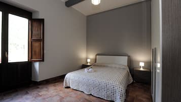 Un dormitorio con cama, dos mesitas de noche con lámparas, una ventana con vistas y una puerta.